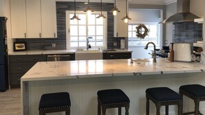 Een moderne keuken met een groot keukenblok, hanglampen en een ingebouwde kookplaat.
