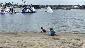 Een zandstrand met een speelzone in het water, inclusief opblaasbare constructies.
