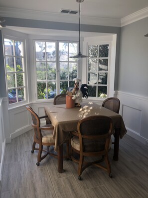 Un comedor con una mesa dispuesta para cuatro personas, rodeada de sillas de mimbre. Amplios ventanales ofrecen vistas al exterior.