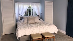 Een slaapkamer met een groot bed, twee nachtkastjes, een raam met gordijnen en een deur.
