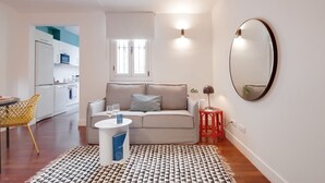 Un salon moderne avec un canapé, une petite table, un tabouret rouge et un miroir rond accroché au mur.