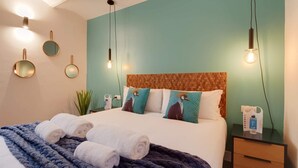 Un lit bien fait, avec des serviettes pliées, une table de chevet sur laquelle se trouvent un téléphone et une bouteille, et un mur orné de trois miroirs ronds.
