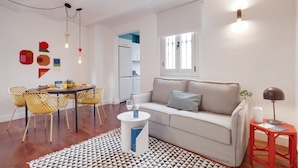 Un salon moderne avec un canapé, une table à manger et des chaises. On aperçoit un coin cuisine à l’arrière-plan.