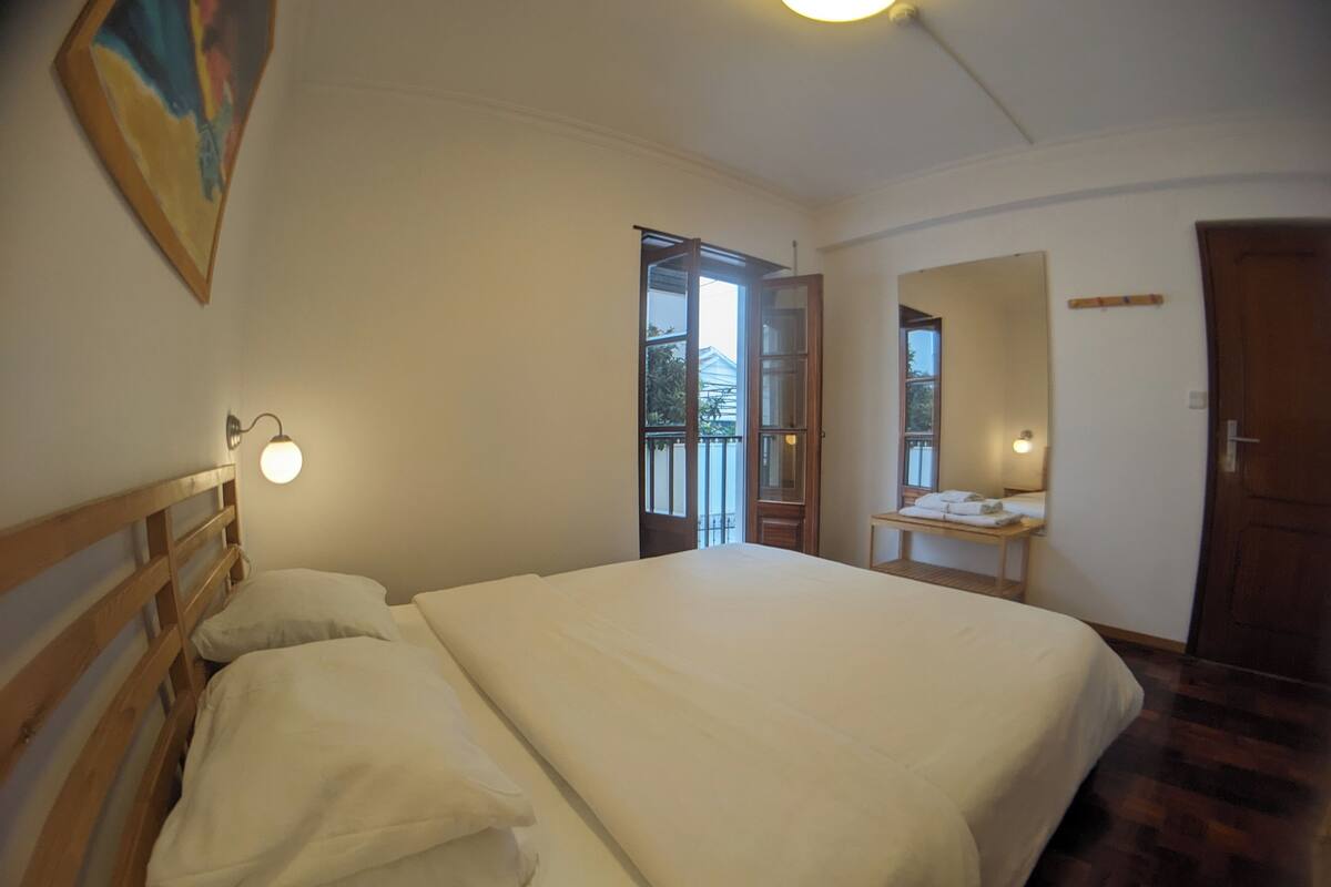 Ein Schlafzimmer mit einem großen Bett, einem Nachttisch mit Lampe, einer Tür und einem Fenster.