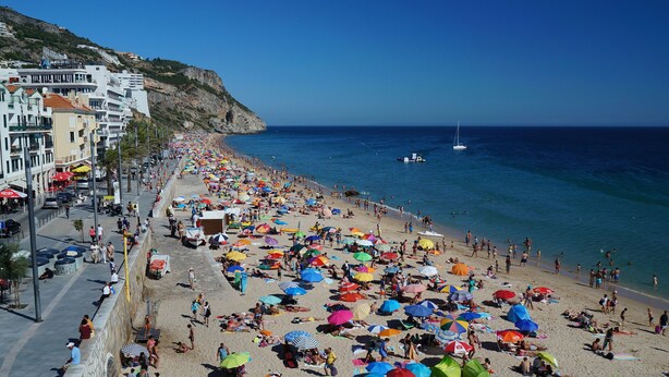 Ein voller Strand mit vielen bunten Sonnenschirmen und Menschen, die das Meer genießen.