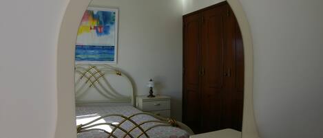 Un dormitorio con una cama, una mesita de noche, una lámpara, un armario de madera y un cuadro en la pared.