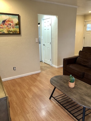 A living room with a brown couch, a wooden coffee table with a cactus, and a painting of a barn on the wall.