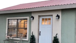 A building with a white door, two potted Christmas trees, a window with blinds, and a small table with chairs outside. - Big Bend Getaway..... (Alpine)