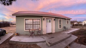 A single-story house with a red roof, a front door, and a window with blinds. There is a small patio with a table and two chairs. - Big Bend Getaway..... (Alpine)