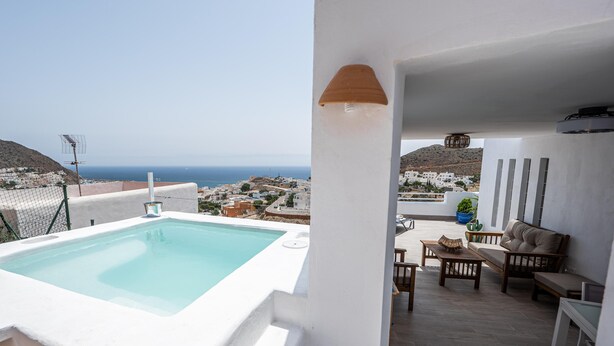 Una terraza en la azotea con piscina, mobiliario exterior y vistas al mar y al pueblo.