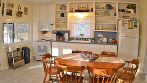 A compact kitchen with white cabinets, a central island, and a dining area with wooden chairs. - Angler Haus , Rustic Wundercove Cottage , Access to Shared Pool and River (New Braunfels)