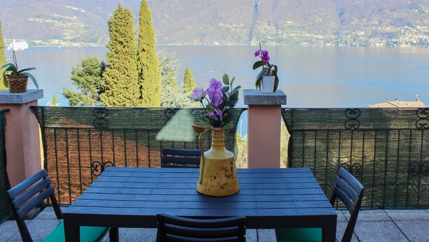 A table with chairs and a vase of flowers, overlooking a lake with mountains in the background. - Sunshine apartment - terrace in Acquaseria (Acquaseria)