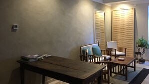 A cozy living room with a wooden table and chairs, a sofa with cushions, and a wall-mounted lamp.