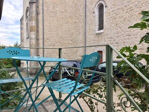 Une table et des chaises en métal bleu sont disposées à l’extérieur, avec un bâtiment en pierre en arrière-plan.