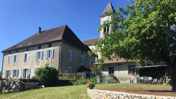 A stone building with a clock tower, surrounded by a stone wall and a grassy area.