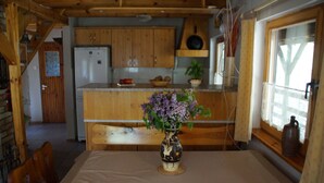 Une cuisine chaleureuse avec des meubles de rangement en bois, un réfrigérateur, une table à manger agrémentée d’un vase de fleurs et une fenêtre avec des rideaux.