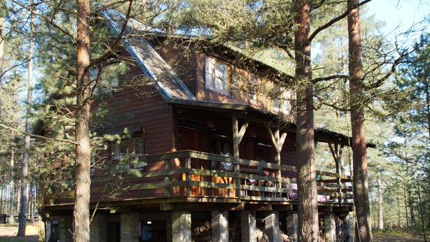 Une cabane avec une façade en bois, un balcon et des fondations en pierre.