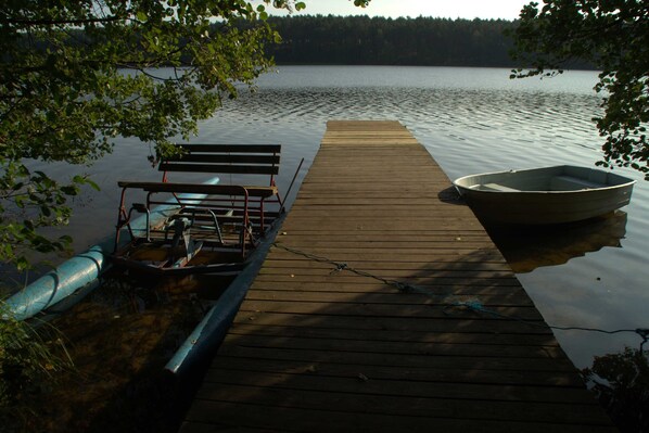 A wooden dock extending into a calm lake, with a bench and a small boat moored at the end.