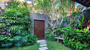 A garden with a stone pathway leading to a wooden door, surrounded by lush tropical plants.