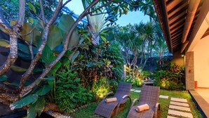 A tropical garden with two lounge chairs, a stone pathway, and lush greenery.