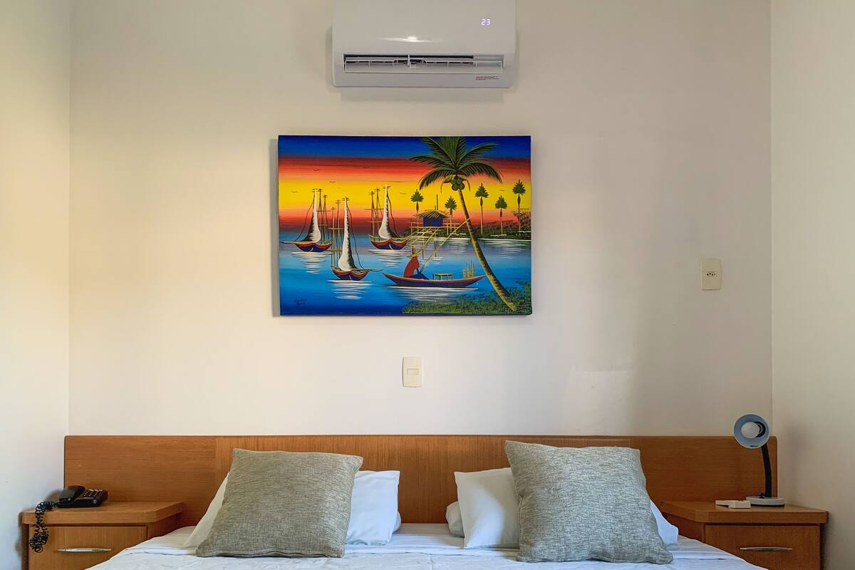 Ein Schlafzimmer mit einem Bett, zwei Nachttischen, einer Wand-Klimaanlage und einem Bild von Segelbooten und Palmen.