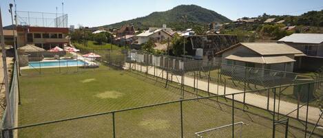 A fenced outdoor area with a pool, a grassy lawn, and a mountain in the background.