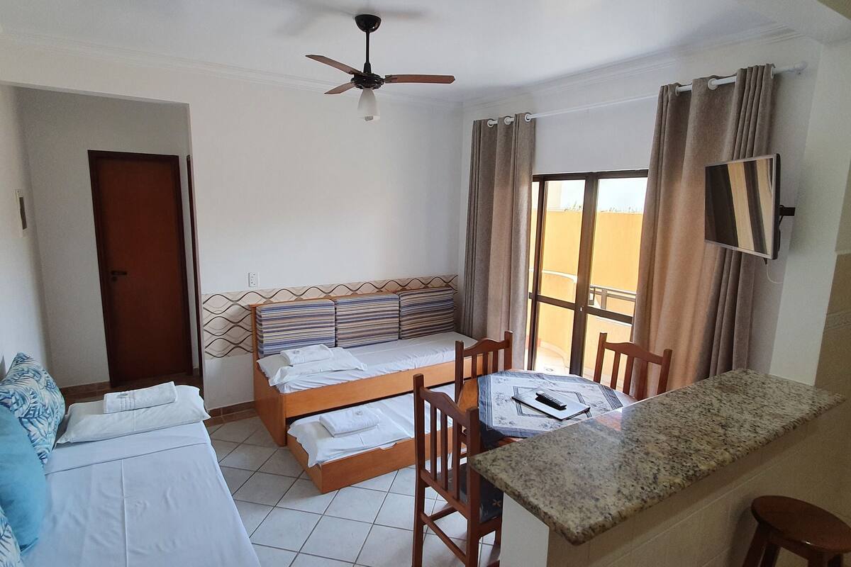 Ein Zimmer mit zwei Betten, einem Esstisch, einem Fernseher und einem Fenster mit Vorhängen.