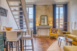 Una sala de estar acogedora con chimenea, suelo de madera, un comedor con sillas, un sillón amarillo y un sofá.
