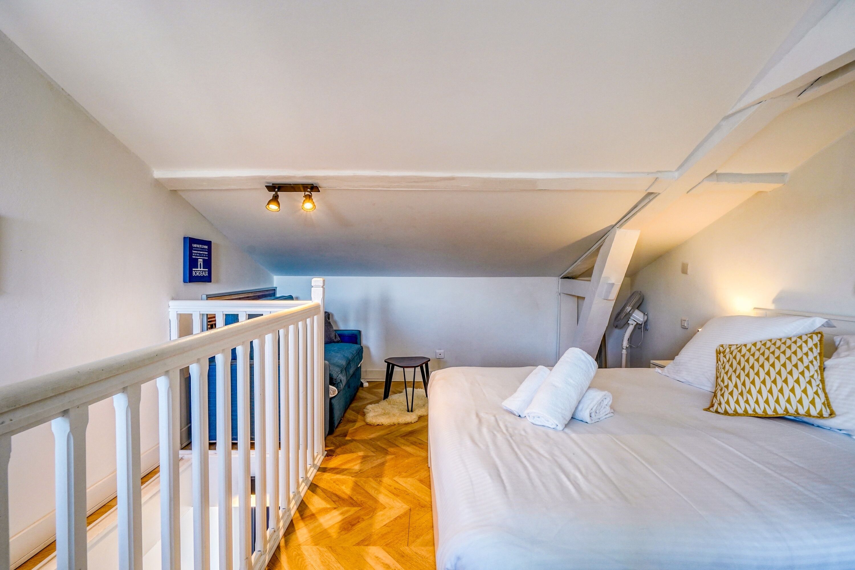 Une chambre à coucher avec un lit, des oreillers blancs, une petite table, un canapé bleu et une balustrade blanche.