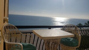Ein Balkon mit Korbstühlen und einem Tisch, mit Blick auf einen Strand, das Meer und Palmen.