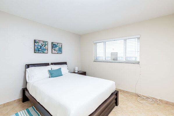 A bedroom with a bed, nightstands, a window, and two wall-mounted artworks.