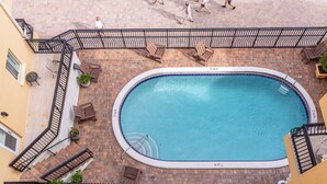 Ein Pool auf dem Dach mit Backsteinboden, umgeben von Holzstühlen und einem Metallgeländer.