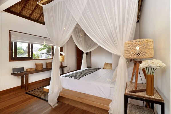 A bedroom with a canopy bed, a bedside lamp, and a view of the outdoors.