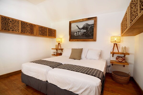 A double bed with a patterned bedspread, two bedside lamps, a wall-mounted picture, and a decorative wooden panel above the bed.