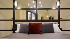 Una cama con colchón gris y blanco, almohada roja y gris, y manta blanca.