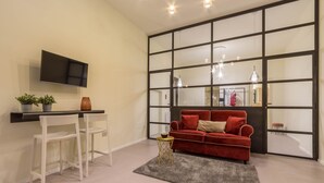 Una sala de estar moderna con un sofá rojo, sillas blancas, una mesita auxiliar y un televisor montado en la pared.