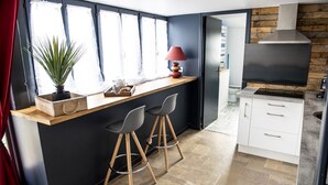 A modern kitchen with a black countertop, two bar stools, a potted plant, and a red lamp.