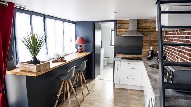 A modern kitchen with a wooden island, bar stools, a red lamp, and a brick wall backsplash.