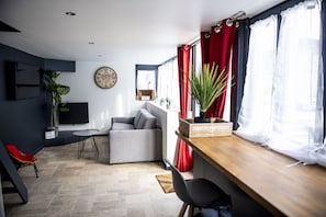A modern living room with a grey sofa, a wooden table, a red chair, and a potted plant.