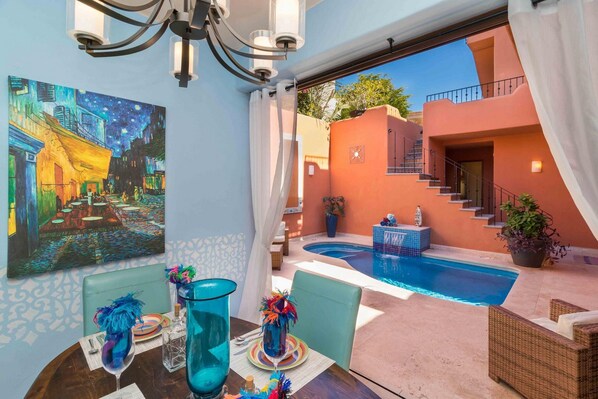 A dining area with a table set for two, a painting of a night scene, and a pool area with a staircase.