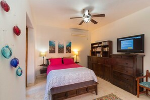 A bedroom with a bed, a ceiling fan, a TV, a bookshelf, and a desk.