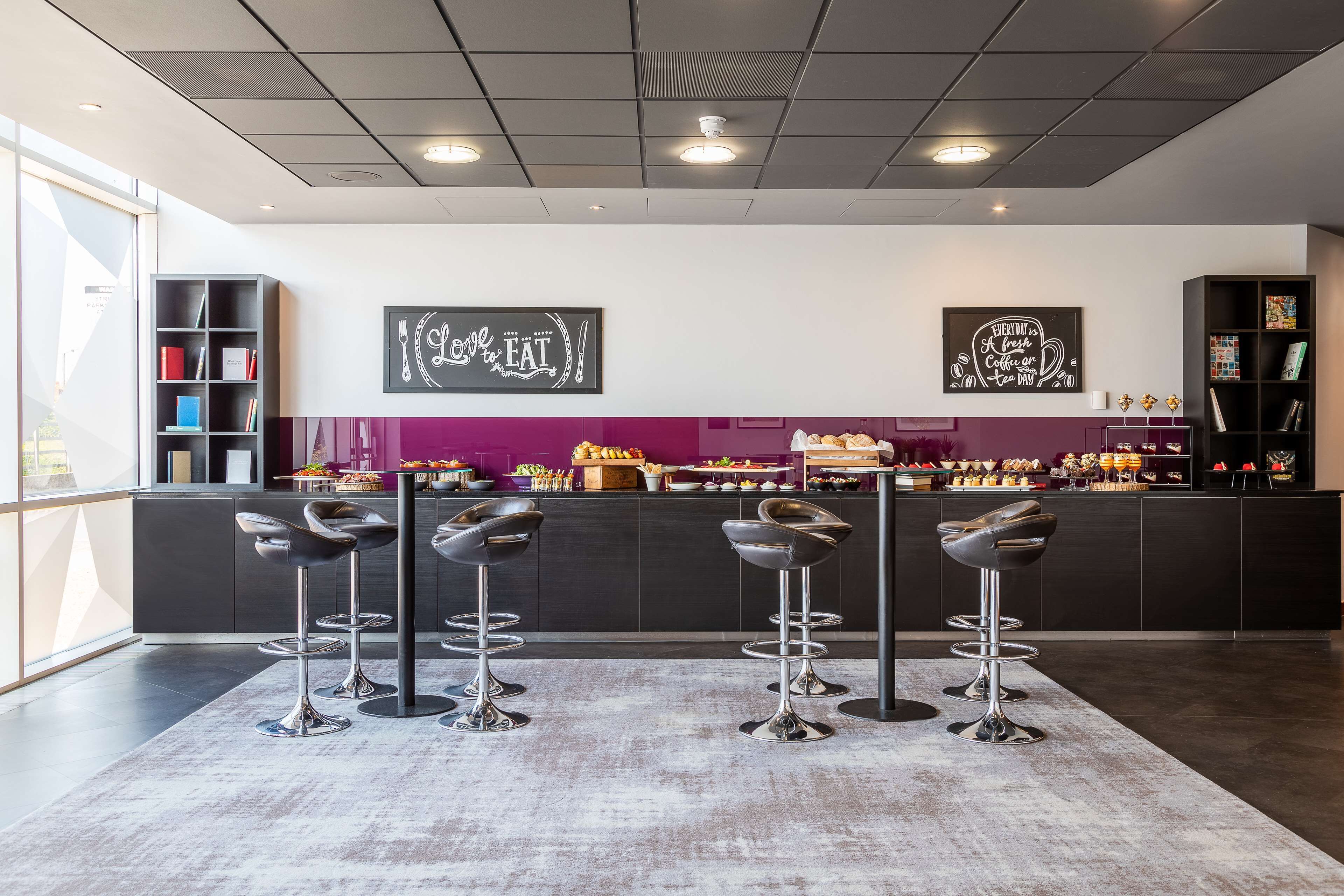 A modern bar area with four stools, a counter with a variety of food items, and two wall art pieces.