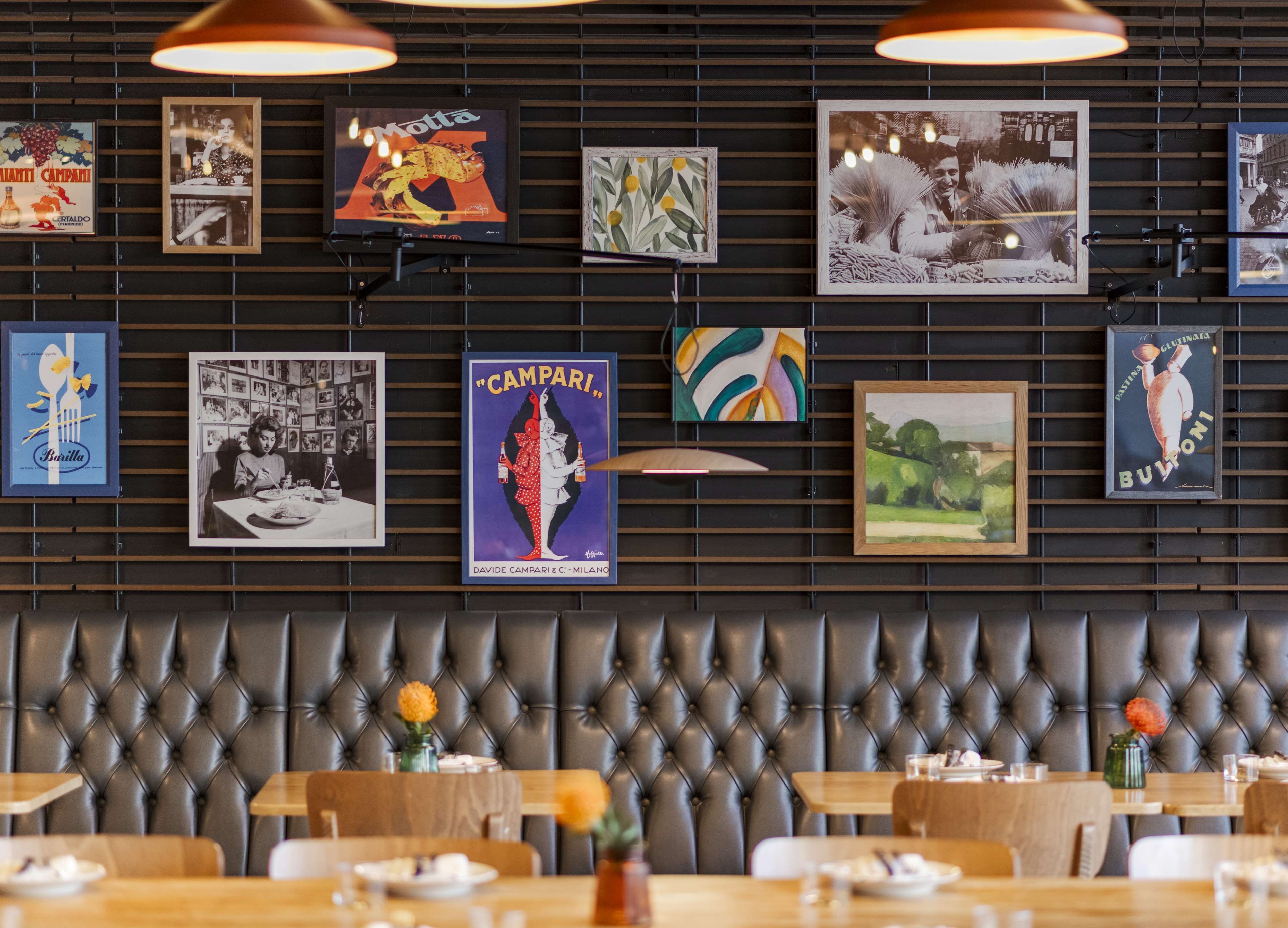 A restaurant interior with a wall of vintage posters, a tufted leather booth seating area, and tables set for dining.