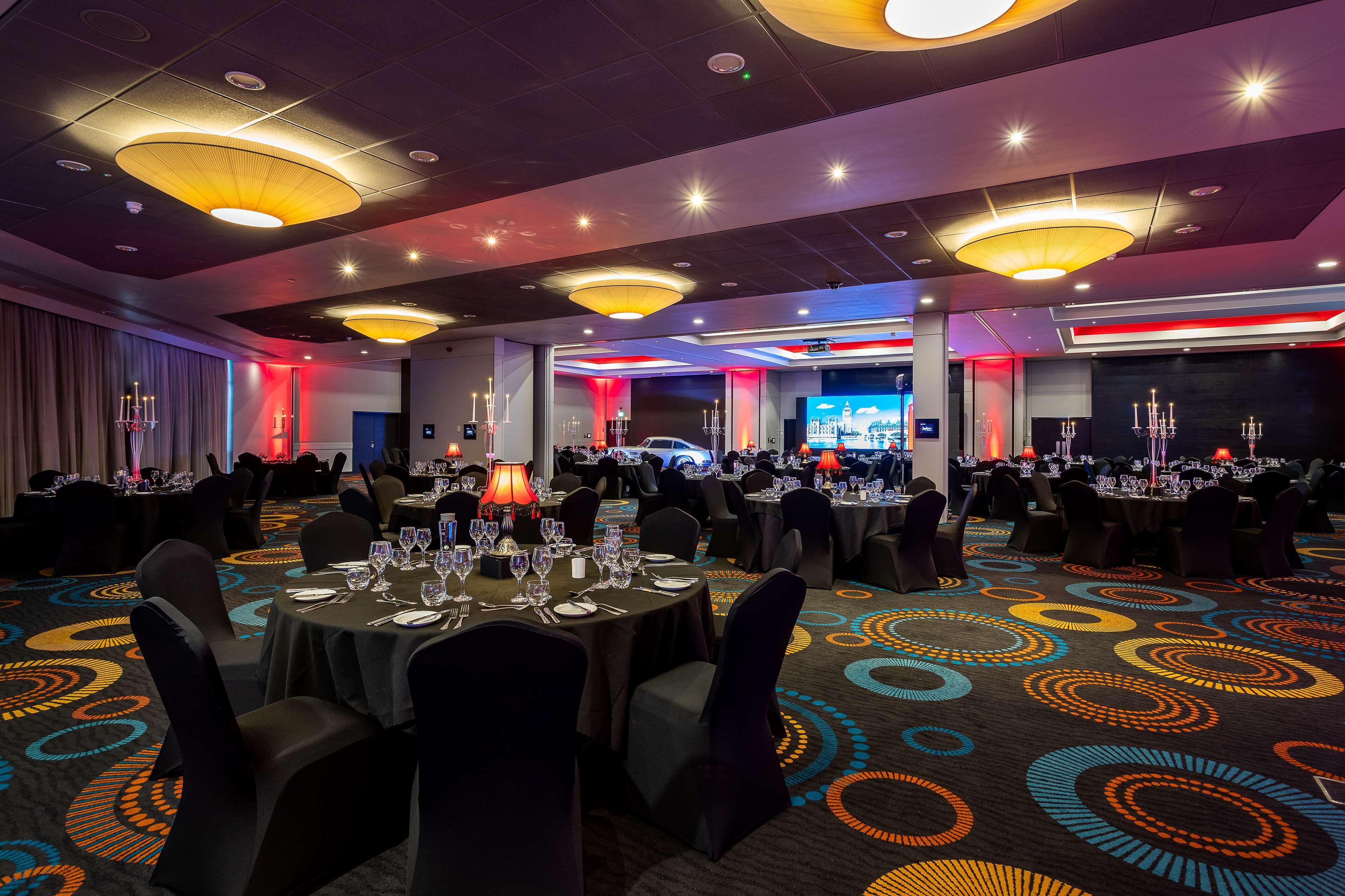 A banquet hall with round tables, chairs, and a carpet with circular patterns.