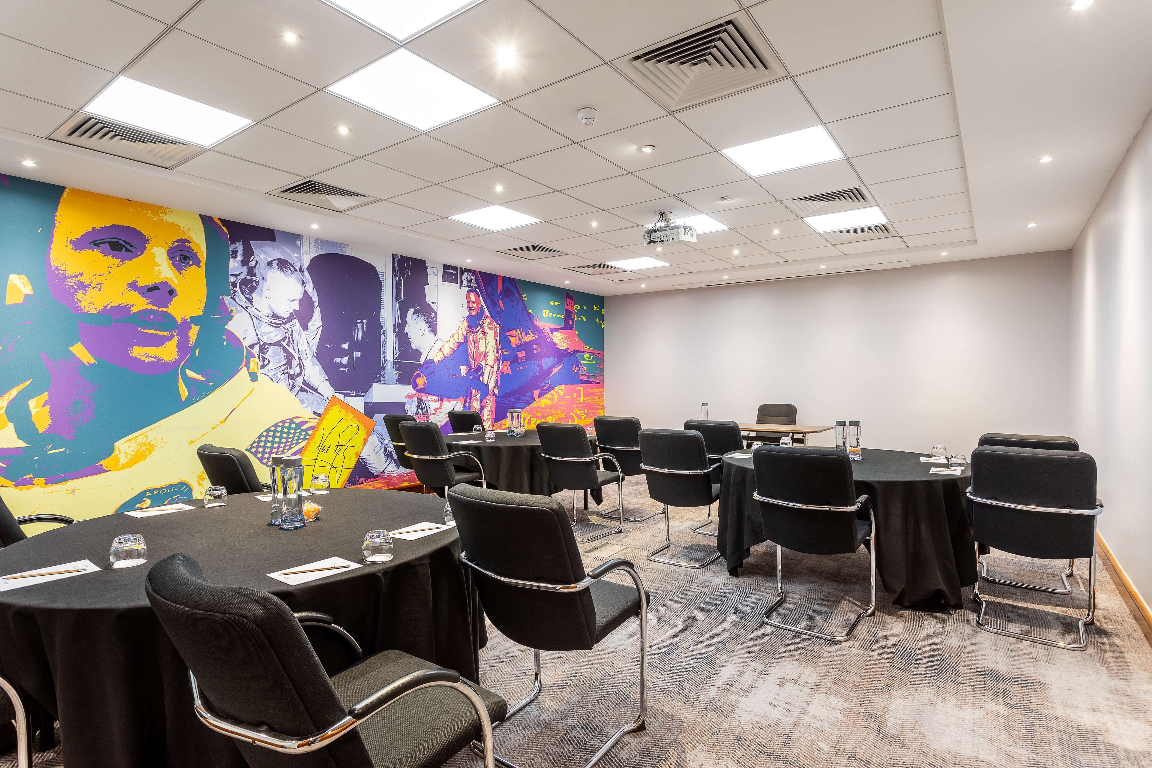 A conference room with round tables, black chairs, and a colorful mural on the wall.