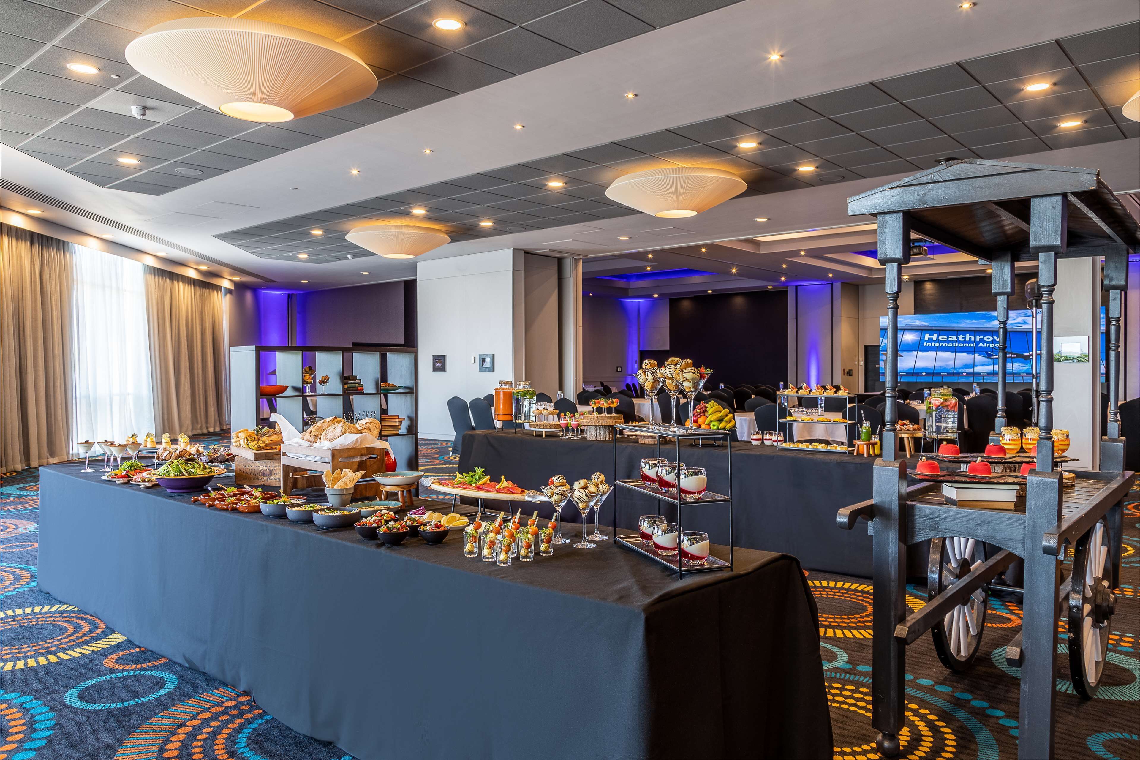 A buffet setup with various food items and a large screen displaying 'Heathrow International Airport'.