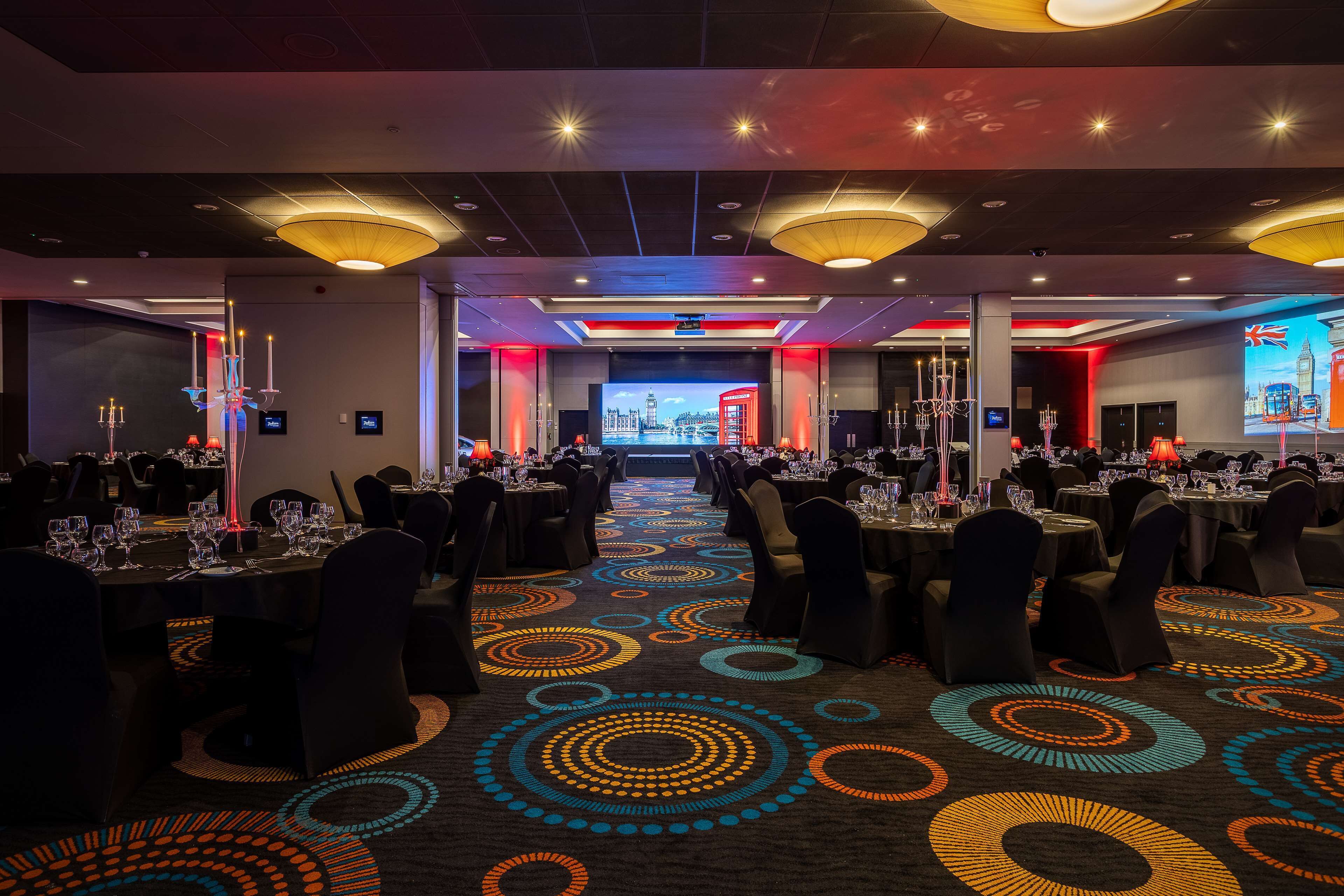 Un salón de banquetes con mesas dispuestas para comer, una alfombra estampada y una pantalla grande que muestra un paisaje urbano.