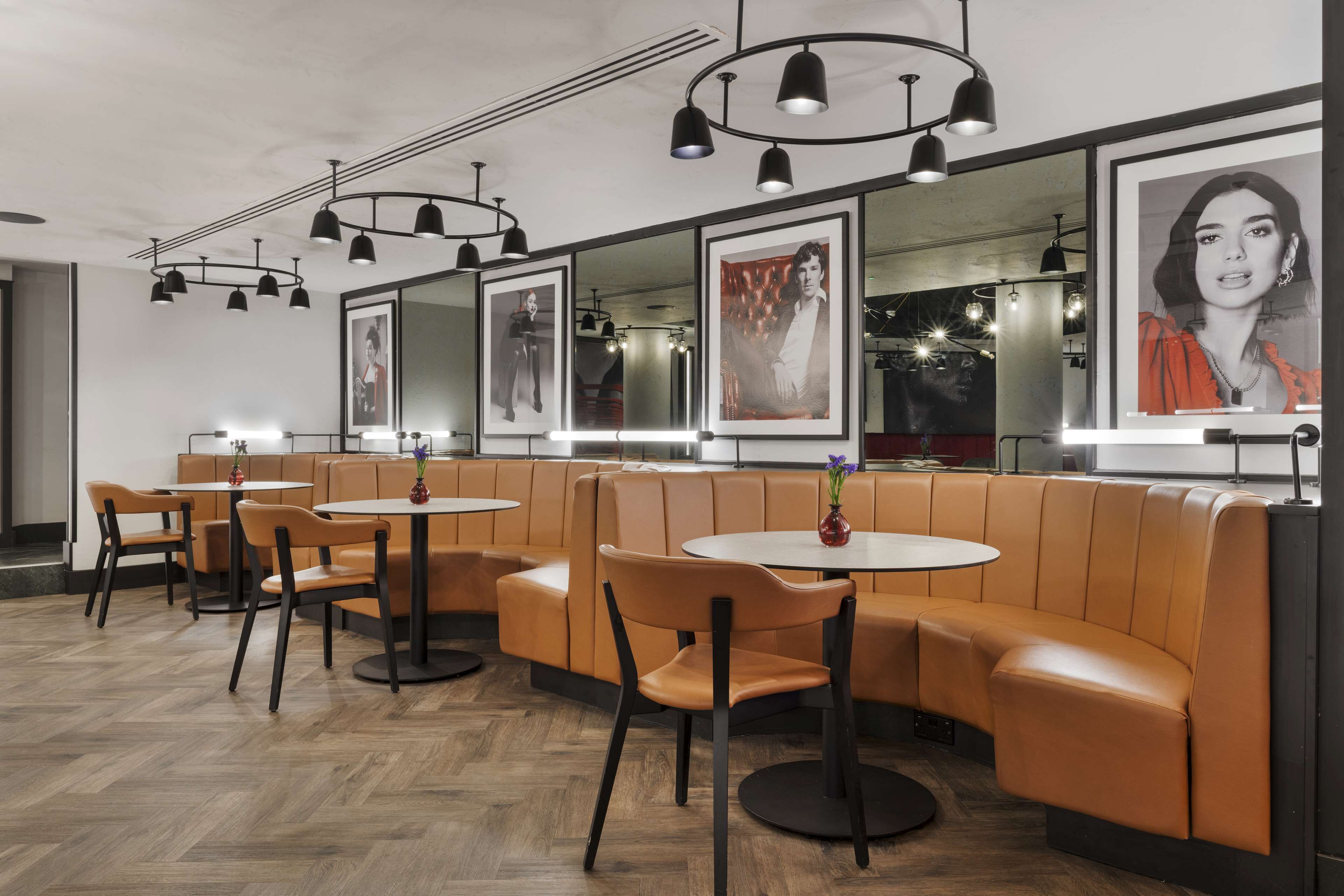 A modern restaurant with leather booths and round tables, featuring pendant lighting and framed artwork on the walls.