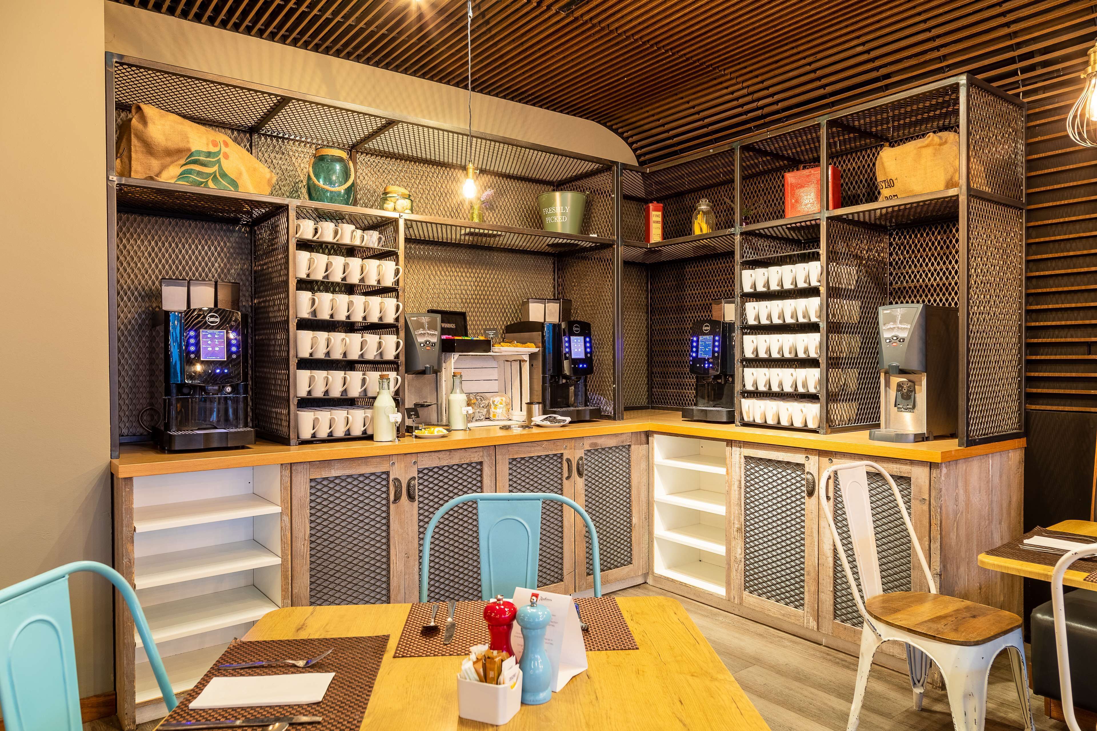 A modern coffee shop with a wooden counter, coffee machines, and a seating area with chairs and a table.