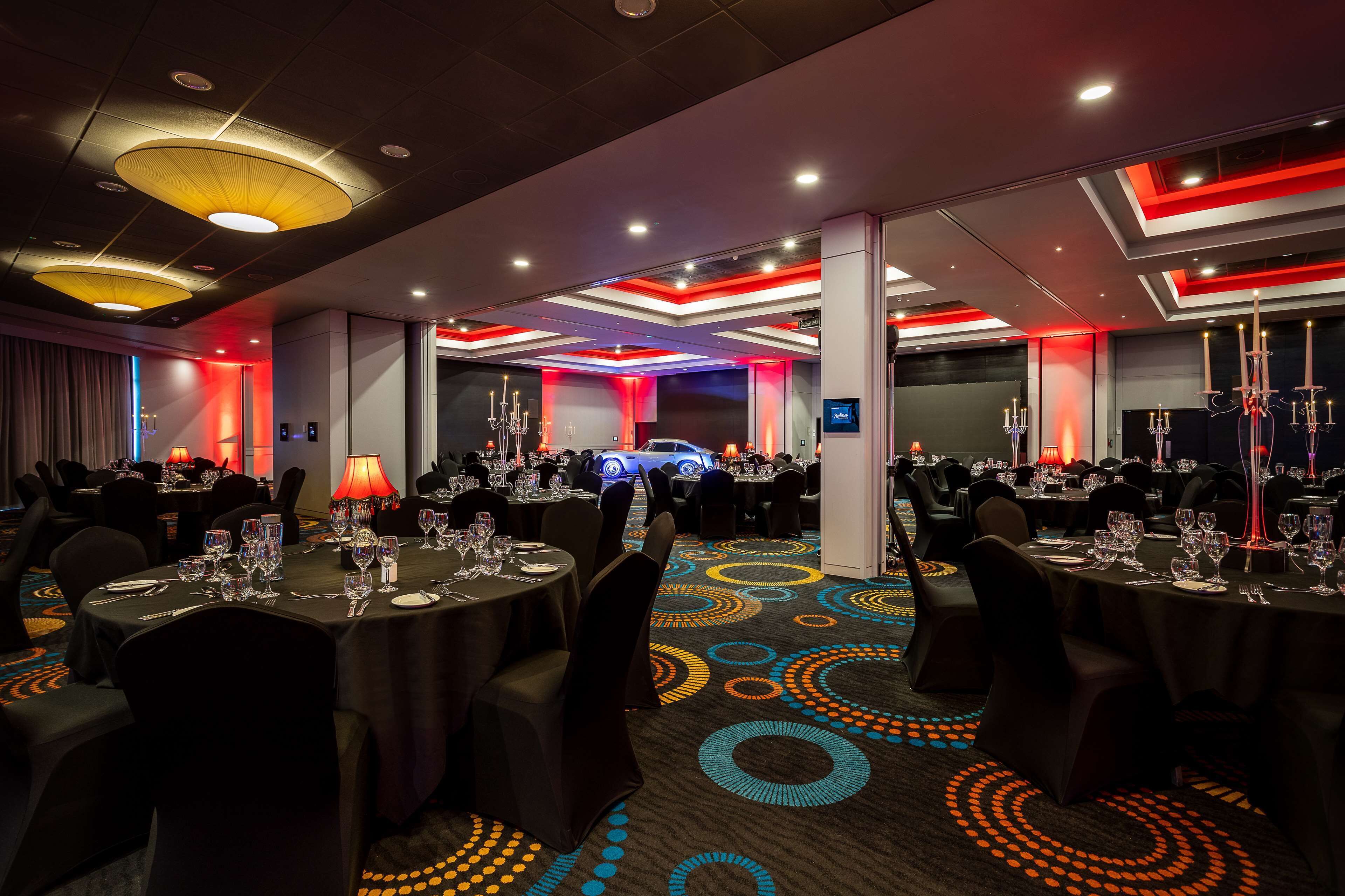 Un comedor de hotel con mesas redondas, sillas y una alfombra con diseños circulares.